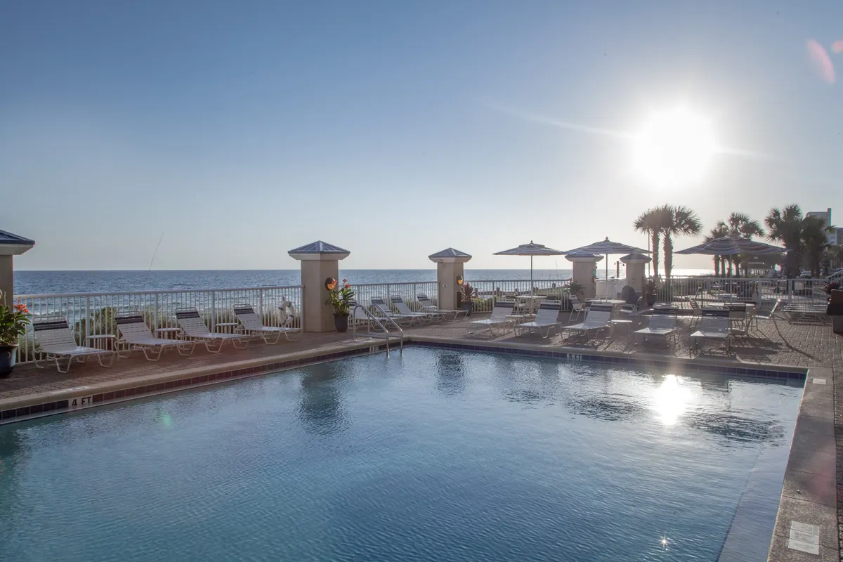 This image presents the outdoor pool area with an inviting ocean view. Poolside lounge chairs and umbrella-shaded tables surround the water, creating a relaxing environment for swimming, sunbathing, and socializing. The scene radiates a vacation vibe, with the beach just steps away beyond the pool.