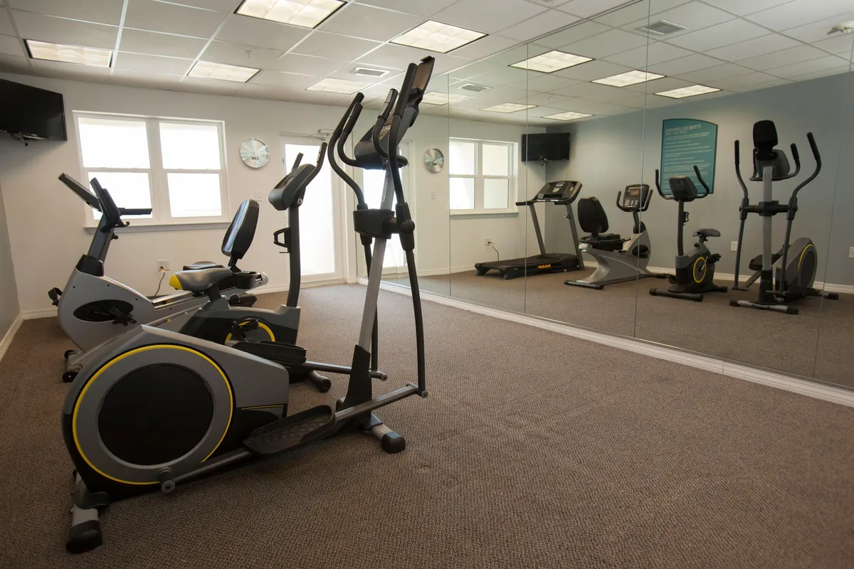 A well-equipped fitness center with advanced elliptical machines, treadmill, and large wall mirrors, creating a motivational atmosphere perfect for guests to maintain their exercise routines while traveling.
